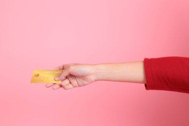 Mutlu Çin Yeni Yılı, kırmızı günlük tişörtlü Asyalı genç bir kadın el ele tutuşup pembe arka planda izole edilmiş kırmızı kredi kartı kullanıyor. Gen Z