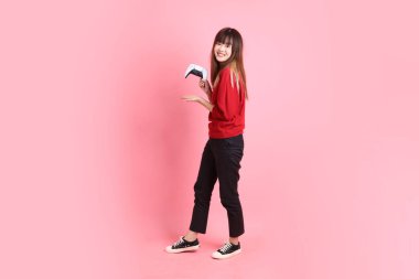 Mutlu Çin Yeni Yılı, kırmızı günlük tişörtlü Asyalı genç bayan kontrolör jesti ya da pembe arka planda izole video oyun konsolu oynuyor. Gen Z