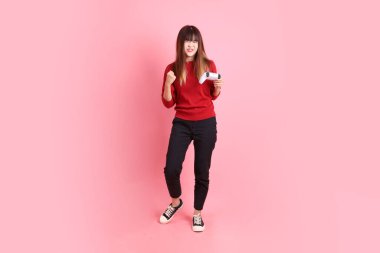 Mutlu Çin Yeni Yılı, kırmızı günlük tişörtlü Asyalı genç bayan kontrolör jesti ya da pembe arka planda izole video oyun konsolu oynuyor. Gen Z