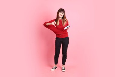 Mutlu Çin Yeni Yılı, kırmızı günlük tişörtlü Asyalı genç bayan kontrolör jesti ya da pembe arka planda izole video oyun konsolu oynuyor. Gen Z