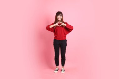 Mutlu Çin Yeni Yılı, kırmızı günlük tişörtlü Asyalı kadın kalp şeklinde jestler, küçük kalp, pembe arka planda izole edilmiş aşk. Gen Z