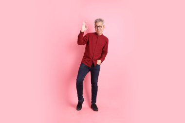 Happy Chinese New Year, asian senior man in formal and casual red shirts with gesture of thumbs up, ok or confirm isolated on pink background. clipart