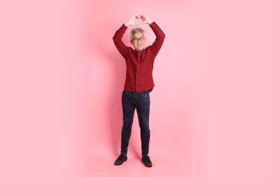 Mutlu Çin Yeni Yılı, resmi ve sıradan kırmızı tişörtlü Asyalı son sınıf öğrencisi. Kalp şeklinde jestler, mini kalp, pembe arka planda izole edilmiş aşk..