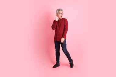 Mutlu Çin Yeni Yılı, resmi ve sıradan kırmızı tişörtlü Asyalı son sınıf öğrencisi pembe arka planda izole edilmiş dinleme ve işitme hareketi ile.