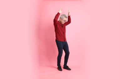 Mutlu Çin Yeni Yılı, resmi ve sıradan kırmızı tişörtlü Asyalı kıdemli dinamik duruşu olan, pembe arka planda izole edilmiş bacağını tekmelerken bağıran adam..