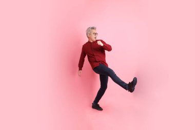 Mutlu Çin Yeni Yılı, resmi ve sıradan kırmızı tişörtlü Asyalı kıdemli dinamik duruşu olan, pembe arka planda izole edilmiş bacağını tekmelerken bağıran adam..