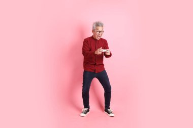 Mutlu Çin Yeni Yılları, resmi ve sıradan kırmızı tişörtlü Asyalı kıdemli adam. Kontrolcü jesti ya da pembe arka planda izole edilmiş video oyun konsolu..