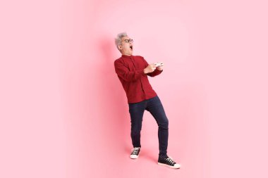 Mutlu Çin Yeni Yılları, resmi ve sıradan kırmızı tişörtlü Asyalı kıdemli adam. Kontrolcü jesti ya da pembe arka planda izole edilmiş video oyun konsolu..