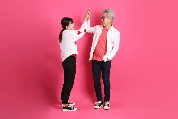 Sevgililer Günü 'nde, Asyalı son sınıf öğrencisi ve genç bayan pembe arka planda izole edilmiş el sıkışma, selamlama, beşlik çakma jesti ve beyaz kalp şeklinde gömlekli gündelik kırmızı kıyafetler giyerler..