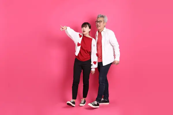 Sevgililer Günü, Asyalı son sınıf öğrencisi ve genç kadın pembe arka planda izole edilmiş yürüyüş jesti ile günlük kırmızı elbiseler ve beyaz kalp şeklinde gömlek giyerler..