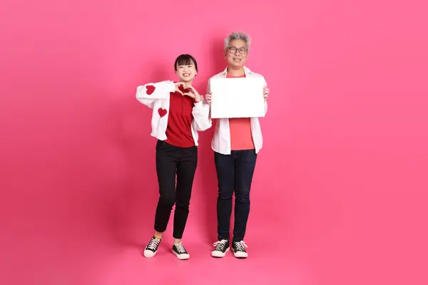 Sevgililer Günü 'nde, Asyalı son sınıf öğrencisi ve genç kadın pembe arka planda boş tuval tutmanın jesti olarak beyaz kalp şeklinde gömlek ve günlük kırmızı kıyafetler giyerler..