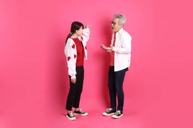 Sevgililer Günü 'nde, Asyalı son sınıf öğrencisi ve genç kadın pembe arka planda izole edilmiş ihtilaf jestleriyle beyaz kalp şeklinde gömlek ve günlük kırmızı kıyafetler giyerler..