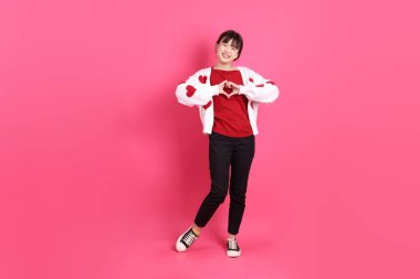 Sevgililer Günü, kırmızı tişörtlü Asyalı bir kadın ya da günlük kıyafetler, kalp şeklinde kırmızı bir gömlek, pembe arka planda izole edilmiş bir aşk jesti. Gen Z