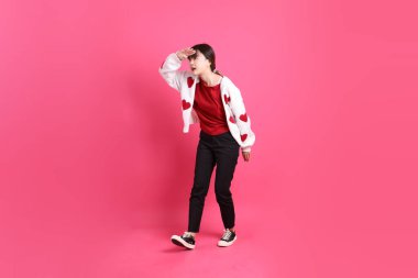 Sevgililer Günü 'nde, kırmızı tişörtlü Asyalı bir kadın ya da günlük kıyafetler, kırmızı kalp şeklinde gömlek, uzaktan bakma jesti, pembe arka planda soyutlanmış görünüyor. Gen Z