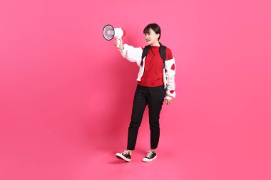 Kırmızı tişörtlü Asyalı kız öğrenci ya da günlük kıyafetler, kırmızı kalp şeklinde gömlek okul çantası taşıyor ve pembe arka planda megafon taşıyor. Gen Z