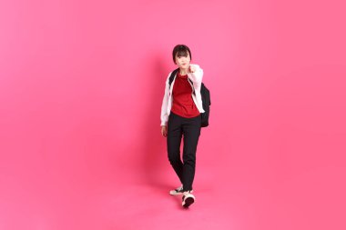 Kırmızı tişörtlü Asyalı kız öğrenci ya da günlük kıyafetler, kırmızı kalp şeklinde gömlek okul çantası taşıyor ve pembe arka planda izole edilmiş bir şekilde selamlanıyor. Gen Z