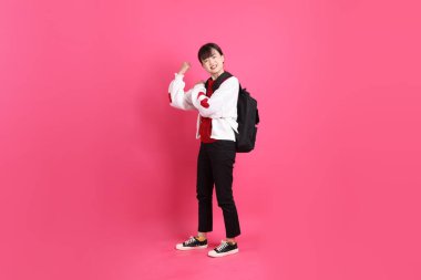 Kırmızı tişörtlü Asyalı kız öğrenci ya da günlük kıyafetler, kırmızı kalp şeklinde gömlek okul çantası taşıyor ve pembe arka planda güçlü, sağlıklı bir jest yapıyor. Gen Z