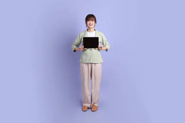 Resmi kıyafetli genç bir Asyalı iş kadını elinde tablet, ayakta duruyor ve gülümsüyor mor arka planda. Gen Z, staj, kariyer, ofis.
