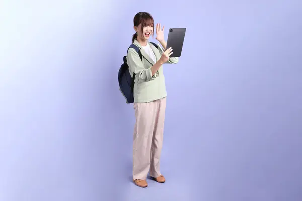 Resmi kıyafetli genç bir Asyalı iş kadını elinde tablet tutarak mor arka planda izole edilmiş bir selfie çekiyor. Gen Z, staj, kariyer, ofis.