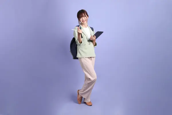 Resmi kıyafetli genç Asyalı iş kadını elinde tablet, kalp şeklinde mini kalp, mor arka planda izole edilmiş aşk jestleriyle. Gen Z, staj, kariyer, ofis.