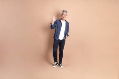 Asyalı son sınıf öğrencisi, sıradan giyinmiş, baş parmağı havada, ya da kahverengi arka planda izole edilmiş, tamam mı? Turist, akıllı gündelik.