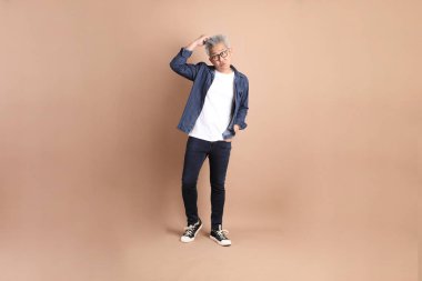 Kahverengi arka planda izole edilmiş bir düşünce jesti olan Asyalı son sınıf öğrencisi. Turist, akıllı gündelik.