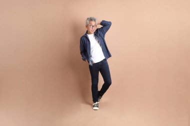 Kahverengi arka planda izole edilmiş bir düşünce jesti olan Asyalı son sınıf öğrencisi. Turist, akıllı gündelik.