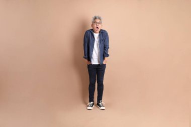 Sürpriz hareketleriyle Asyalı son sınıf öğrencisi ve kahverengi arka planda etkileyici bir izolasyon. Turist, akıllı gündelik.