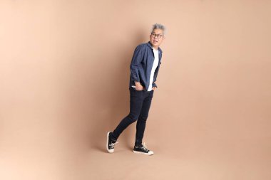 Kahverengi arka planda izole edilmiş yürüyüş jesti olan Asyalı son sınıf öğrencisi. Turist, akıllı gündelik.