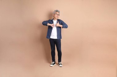 Kahverengi arka planda izole edilmiş, üst düzey Asyalı bir adam. Turist, akıllı gündelik.