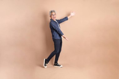 Kahverengi arka planda izole edilmiş, günlük kıyafetli Asyalı bir adam. Turist, akıllı gündelik.