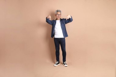 Kahverengi arka planda izole edilmiş, günlük kıyafetli Asyalı bir adam. Turist, akıllı gündelik.