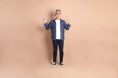 Kahverengi arka planda izole edilmiş, günlük kıyafetli Asyalı bir adam. Turist, akıllı gündelik.