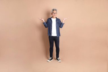 Kahverengi arka planda izole edilmiş, günlük kıyafetli Asyalı bir adam. Turist, akıllı gündelik.