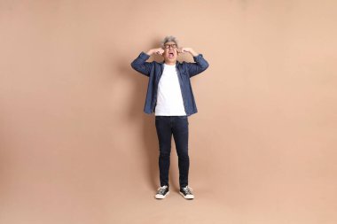 Hayal kırıklığı jesti ile Asyalı son sınıf öğrencisi kahverengi arka planda izole edilmiş ağlıyordu. Turist, akıllı gündelik.