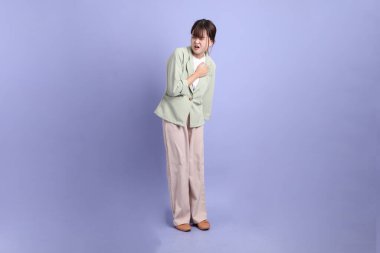 Mor arka planda izole edilmiş göğüs ağrısı jesti ile resmi giyinmiş Asyalı genç bir iş kadını. Gen Z, staj, kariyer, ofis.