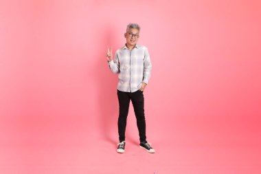 Barış işareti olan resmi ve günlük beyaz gömlekli Asyalı son sınıf öğrencisi. Pembe arka planda iki parmak izole edilmiş..