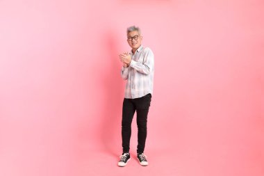 Pembe arka planda el çırpma hareketi yapan resmi ve gündelik beyaz gömlekli Asyalı kıdemli bir adam..