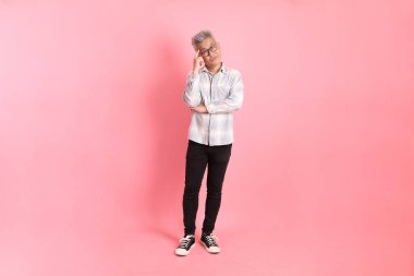 Pembe arka planda soyutlanmış düşünce jesti olan resmi ve günlük beyaz gömlekli Asyalı kıdemli bir adam..