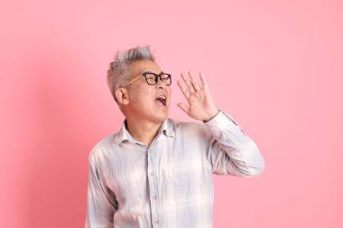 Pembe arka planda izole edilmiş bağrışmaları olan resmi ve günlük beyaz gömlekli Asyalı kıdemli adam..