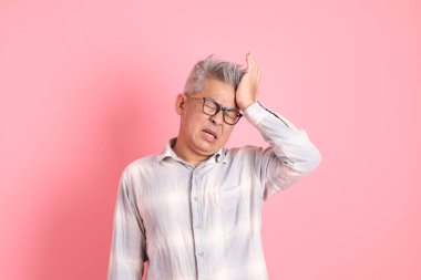 Baş ağrısı jesti ya da pembe arka planda izole edilmiş stresi olan resmi ve günlük beyaz gömlekli Asyalı kıdemli bir adam..