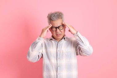 Baş ağrısı jesti ya da pembe arka planda izole edilmiş stresi olan resmi ve günlük beyaz gömlekli Asyalı kıdemli bir adam..