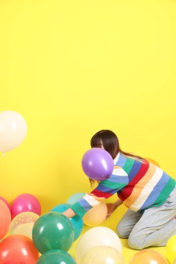 Renkli kışlık elbiseler giyen Asyalı bir kadın. Renkli balonla oynama jesti. Sarı balonla izole edilmiş. Gen Z