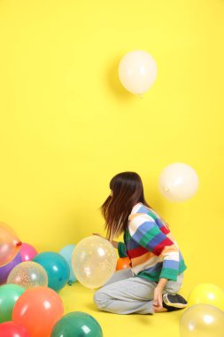 Renkli kışlık elbiseler giyen Asyalı bir kadın. Renkli balonla oynama jesti. Sarı balonla izole edilmiş. Gen Z