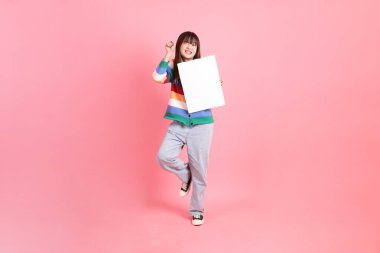 Renkli gökkuşağı kıyafetleri giyen Asyalı bir kadın ya da pembe arka planda boş tuval tutan bir jest. Gen Z