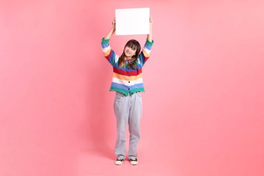 Renkli gökkuşağı kıyafetleri giyen Asyalı bir kadın ya da pembe arka planda boş tuval tutan bir jest. Gen Z