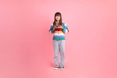 Renkli gökkuşağı kıyafetleri giyen Asyalı bir kadın ya da pembe arka planda saklanmış hediye kutusunu tutan bir jest. Gen Z