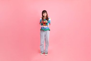 Renkli gökkuşağı kıyafetleri giyen Asyalı bir kadın ya da pembe arka planda saklanmış hediye kutusunu tutan bir jest. Gen Z