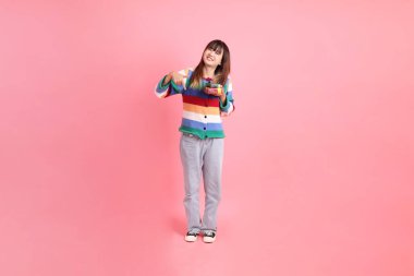 Renkli gökkuşağı kıyafetleri giyen Asyalı bir kadın ya da pembe arka planda izole edilmiş bir şekilde duran hediye kutusunu tutan sıradan görünüşlü bir kadın. Gen Z