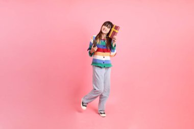 Renkli gökkuşağı kıyafetleri giyen Asyalı bir kadın ya da pembe arka planda saklanmış hediye kutusunu tutan bir jest. Gen Z